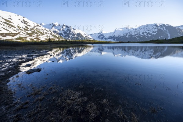 Mountain peaks with Portage Glacier glacier and snow reflected in Divide Lake mountain lake in evening light, Portage Pass Trail, Whittier, Alaska, USA