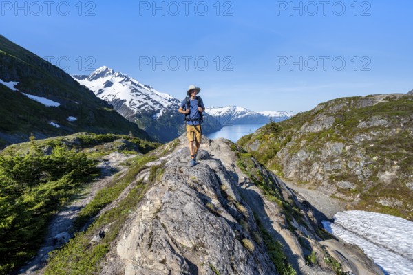 Hikers on Portage Pass, snow-covered mountains and Fjord Passage Canal, near Whittier, Alaska, USA