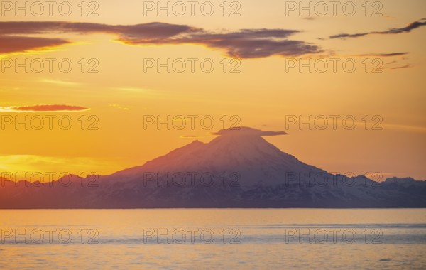 View of Cook Inlet on white mountain peaks of Mount Redoubt at sunset, picturesque golden light of the midnight sun, mountains of the Aleutian Range, Anchor Point, Anchor River State Recreation Area, Alaska, USA