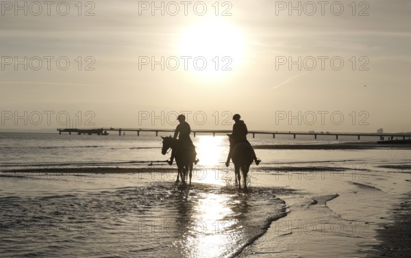 Two female riders ride their horses through the shallow water of the Baltic Sea at sunrise, Scharbeutz, 29.11.2025, Scharbeutz, Schleswig-Holstein, Germany
