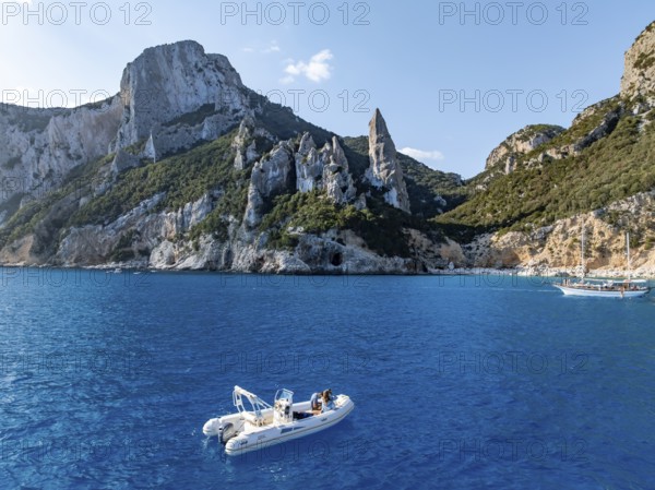 Motor boat off picturesque rocky coast, cliffs with L'Aguglia pinnacle, blue sea and Cala Goloritzé beach, aerial view, Golfo di Orosei, Baunei, Sardinia, Italy