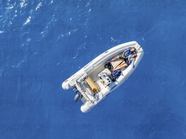 Young woman and young man lying in a motor boat on a blue sea, top-down, aerial view, Golfo di Orosei, Baunei, Sardinia, Italy