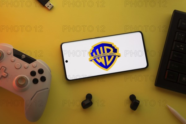 Dhaka, Bangladesh- 22 Mar 2025: Smartphone with Warner Bros. Games, game controller, and earbuds on a pink background
