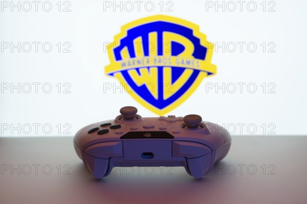 Dhaka, Bangladesh- 14 Nov 2025: A close-up of a white gamepad with the Warner Bros. Games seen on screen in the background