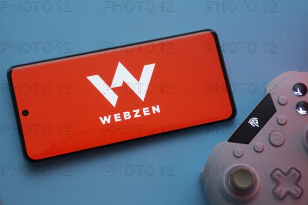 Dhaka, Bangladesh- 22 Mar 2025: Smartphone with Webzen logo, game controller, and earbuds on a background