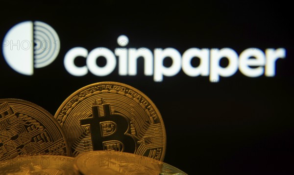 Dhaka, Bangladesh- 19 Sep 2025: Close-up of Bitcoin coins with the Coinpaper logo visible on a screen in the background