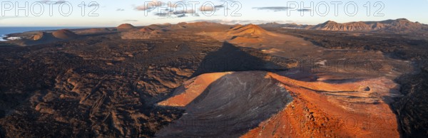 Picturesque volcanic landscape in evening light, red volcano Montaña Bermeja between lava fields, aerial view, Lanzarote, Canary Islands, Spain
