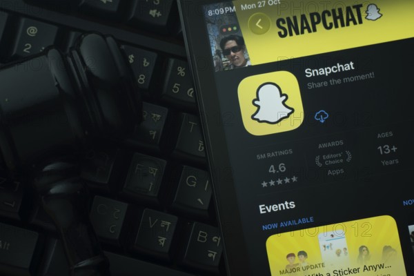 Dhaka, Bangladesh- 28 Oct 2025: An iPad displaying the Snapchat app against a judge's gavel and dark keyboard background