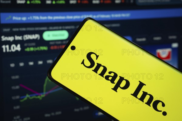 Dhaka, Bangladesh- 18 March 2025: Snap Inc logo is displayed on a smartphone screen, with a stock graph webpage visible on a computer screen in the background