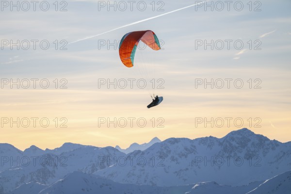 Paragliders flying over snowy mountain peaks in winter in evening light, Kitzbühel Alps, Tyrol, Austria