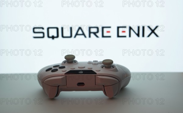Dhaka, Bangladesh- 14 Nov 2025: A close-up of a white gamepad with the Square Enix seen on screen in the background