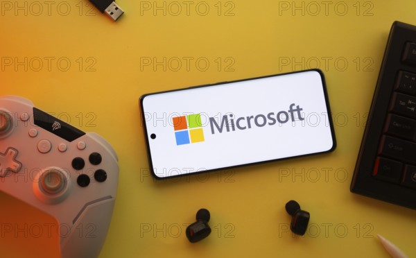 Dhaka, Bangladesh- 23 Mar 2025: Smartphone with Microsoft logo, game controller, and earbuds on a yellow background