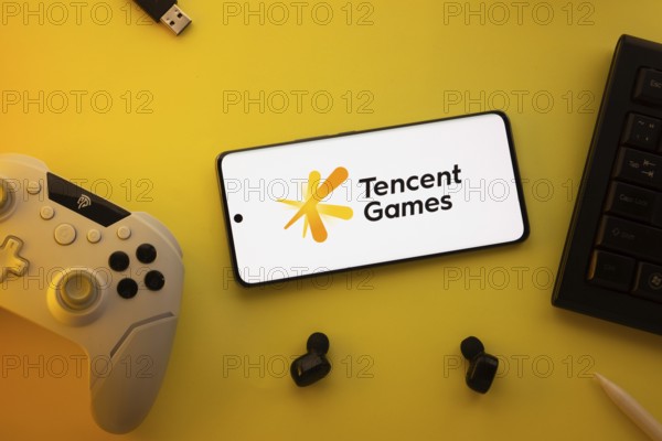 Dhaka, Bangladesh- 23 Mar 2025: Smartphone with Tencent Games logo, game controller, and earbuds on a yellow background