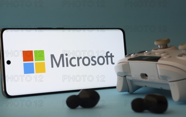 Dhaka, Bangladesh- 23 Mar 2025: A smartphone with a Microsoft icon next to a controller and earbuds on a blue surface