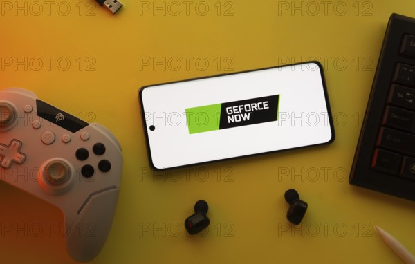 Dhaka, Bangladesh- 23 Mar 2025: Smartphone with Geforce Now logo, game controller, and earbuds on a yellow background