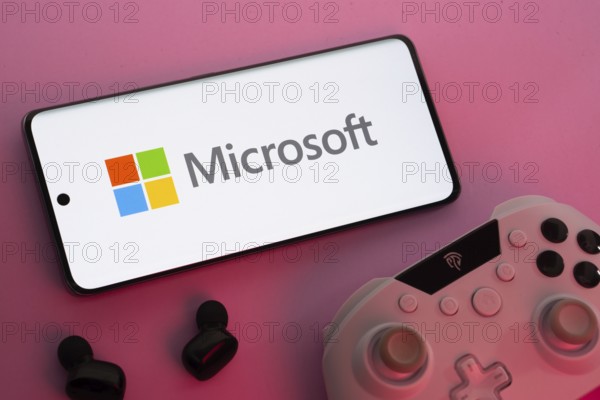 Dhaka, Bangladesh- 22 Mar 2025: Smartphone with Microsoft logo, game controller, and earbuds on a pink background