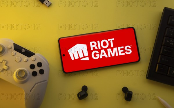 Dhaka, Bangladesh- 23 Mar 2025: Smartphone with Riot Games logo, game controller, and earbuds on a yellow background