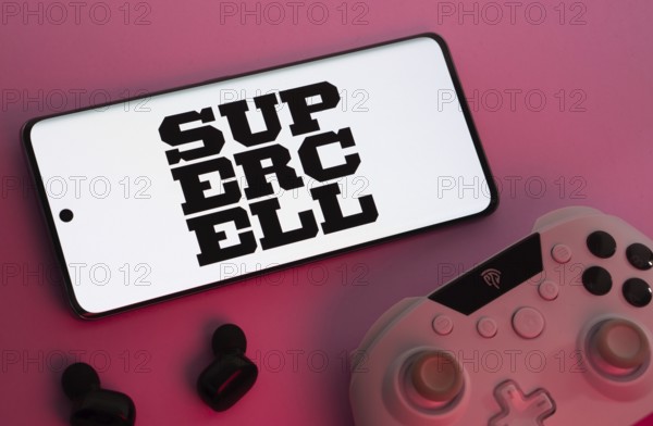 Dhaka, Bangladesh- 22 Mar 2025: Smartphone with Supercell logo, game controller, and earbuds on a pink background