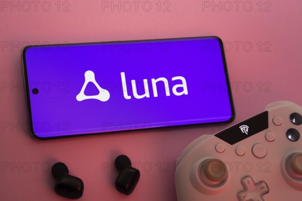 Dhaka, Bangladesh- 22 Mar 2025: Smartphone with Amazon Luna logo, game controller, and earbuds on a pink background