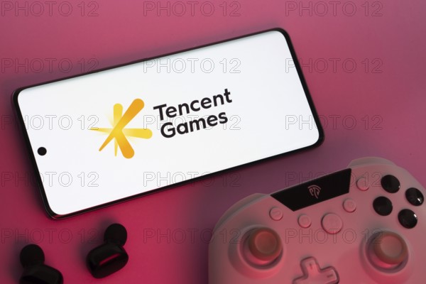 Dhaka, Bangladesh- 22 Mar 2025: Smartphone with Tencent Games logo, game controller, and earbuds on a pink background