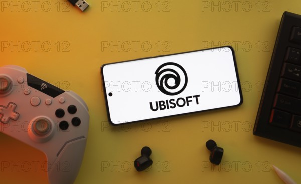 Dhaka, Bangladesh- 23 Mar 2025: Smartphone with Ubisoft logo, game controller, and earbuds on a yellow background