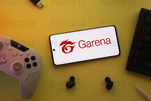 Dhaka, Bangladesh- 23 Mar 2025: Smartphone with Garena logo, game controller, and earbuds on a yellow background