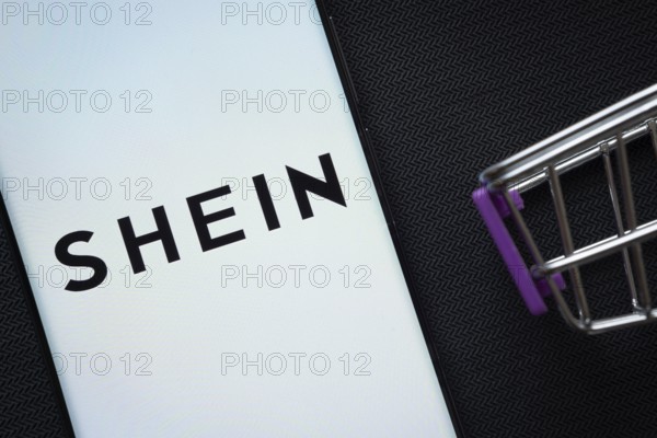 Dhaka, Bangladesh- 03 July 2025: A smartphone displaying the SHEIN logo next to a miniature shopping cart on a background