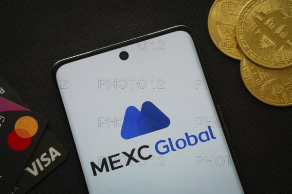 Dhaka, Bangladesh- 06 Sep 2025: Smartphone displaying MEXC Global logo surrounded by Bitcoin coins and payment cards