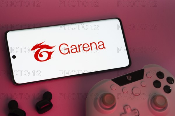 Dhaka, Bangladesh- 22 Mar 2025: Smartphone with Garena logo, game controller, and earbuds on a pink background