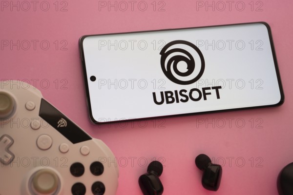 Dhaka, Bangladesh- 22 Mar 2025: Smartphone with Ubisoft logo, game controller, and earbuds on a pink background