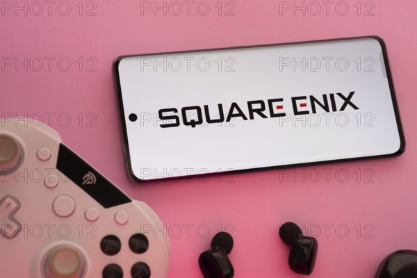 Dhaka, Bangladesh- 22 Mar 2025: Smartphone with Square Enix logo, game controller, and earbuds on a pink background