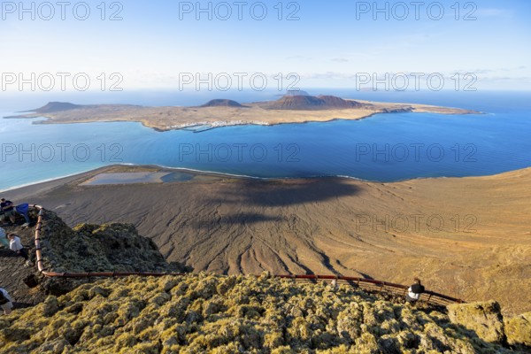 View of La Graciosa island with volcanic craters in the evening light, tourists on an observation deck at the Mirador del Río viewpoint designed by artist César Manrique, Lanzarote, Canary Islands, Spain