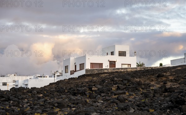 Black coast of volcanic rocks behind typical white houses of the village of La Santa, at sunset, Lanzarote, Canary Islands, Spain