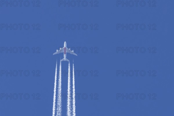 Airbus A380 jet passenger aircraft of Emirates airlines flying in a blue sky with contrails or vapour trails behind, England, United Kingdom