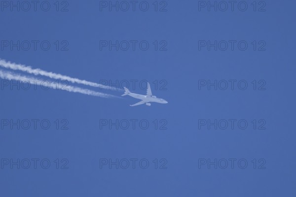 Jet passenger aircraft flying in a blue sky with contrails or vapour trails behind, England, United Kingdom