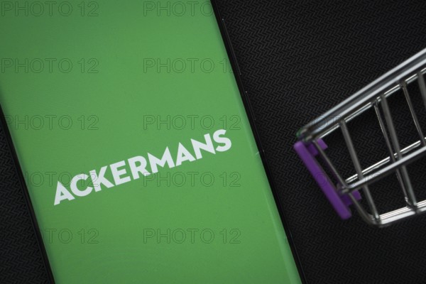 Dhaka, Bangladesh- 03 July 2025: A smartphone displaying the Ackermans logo next to a miniature shopping cart on a background