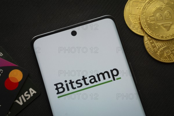 Dhaka, Bangladesh- 06 Sep 2025: Smartphone displaying Bitstamp logo surrounded by Bitcoin coins and payment cards