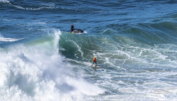 Surfers with their jet ski pilots in the Atlantic waves below Farol de Nazaré, Forte São Miguel, known as a surfer hot spot with monster waves between November and February of each year, Nazaré, Portugal