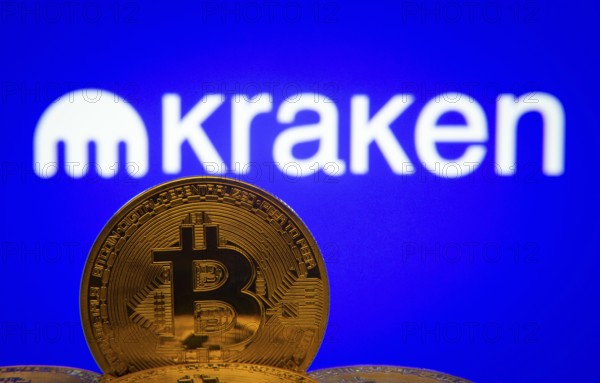 Dhaka, Bangladesh- 01 Nov 2025: Close-up of Bitcoin coins with the Kraken logo visible on a screen in the background
