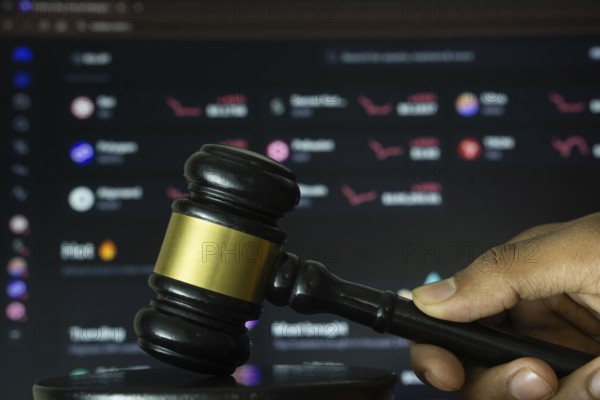 Dhaka, Bangladesh- 20 June 2025: A hand holds a gavel in front of a computer screen displaying Kraken's website