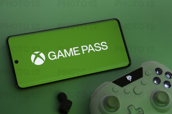Dhaka, Bangladesh- 15 July 2025: Smartphone with Xbox Game Pass logo, game controller, and earbuds on a green background