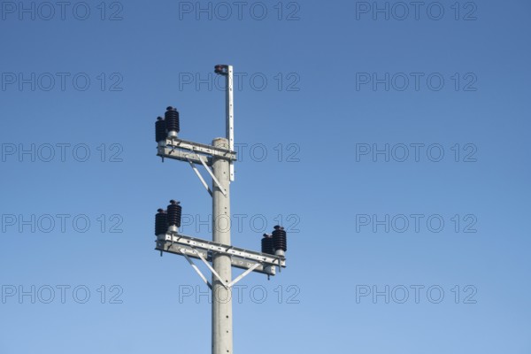 An electric pole with insulators and wires set against a clear blue sky on a bright day