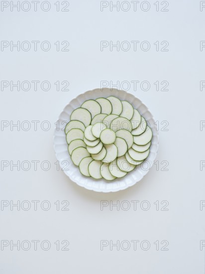 Thinly sliced zucchini arranged on a white plate, forming a visually appealing pattern of concentric circles