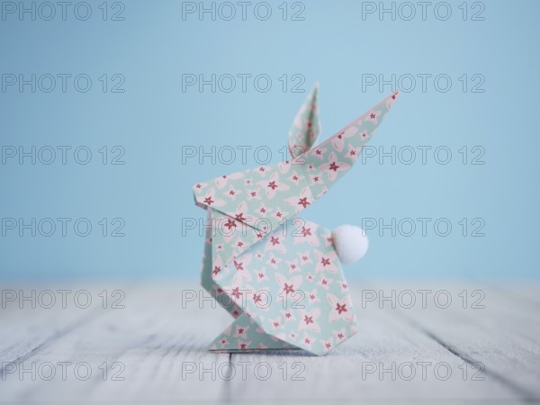 Floral origami easter bunny standing on a white wooden table with a light blue background