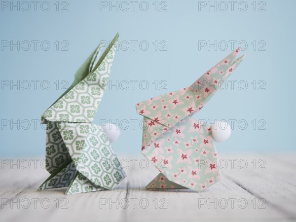 Two colorful origami bunnies standing on a white wooden table with a light blue background, perfect for easter decorations