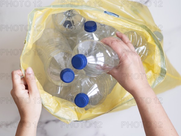 Woman putting used plastic bottles into yellow garbage bag, top view, recycling concept