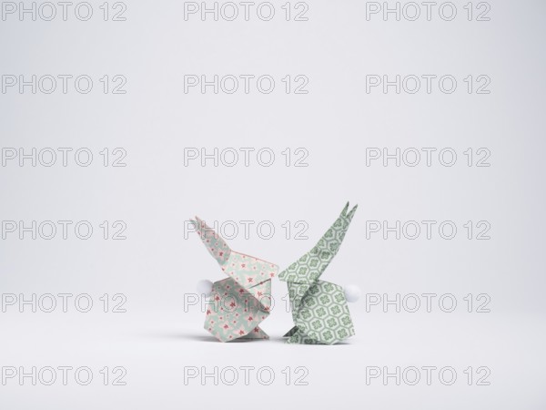 Two origami bunnies made with patterned paper are facing each other on a white background