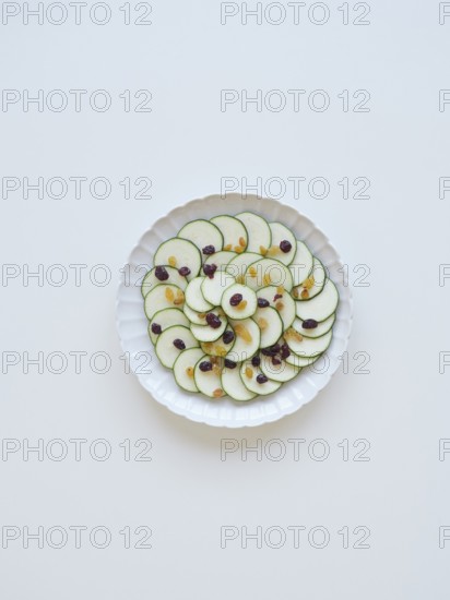 Thinly sliced zucchini arranged on a white plate, garnished with raisins and cranberries, creating a visually appealing and healthy dish
