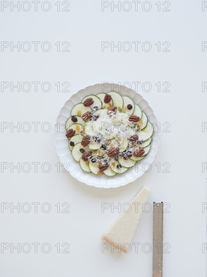 Delicious zucchini carpaccio with parmesan cheese, pecan nuts, raisins and cranberries served on white plate