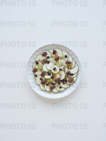 Sliced zucchini arranged on a white plate, creating a carpaccio with raisins and pecans, forming a healthy and visually appealing dish